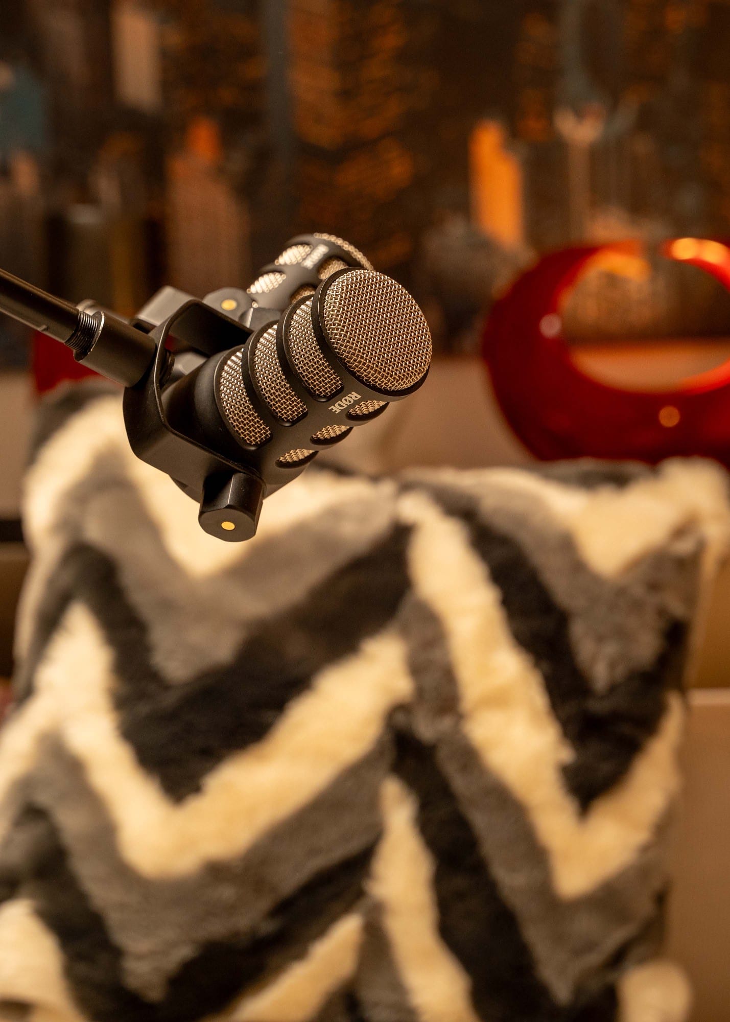 Close-up of a RØDE PodMic on a boom arm above a grey and cream chevron cushion