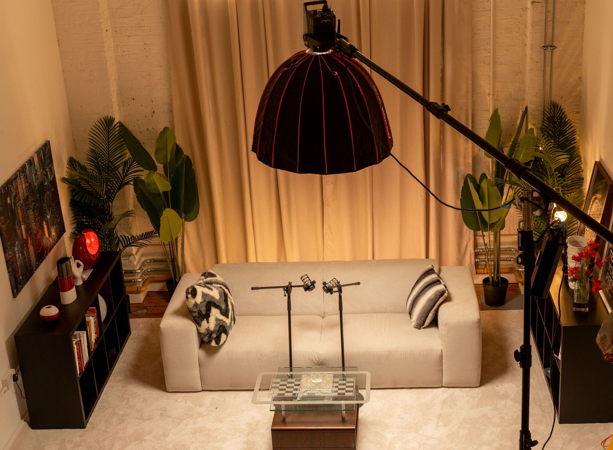 The room seen from above with a large softbox on a boom arm over the sofa, two mic stands and the glass chessboard table on a cream rug
