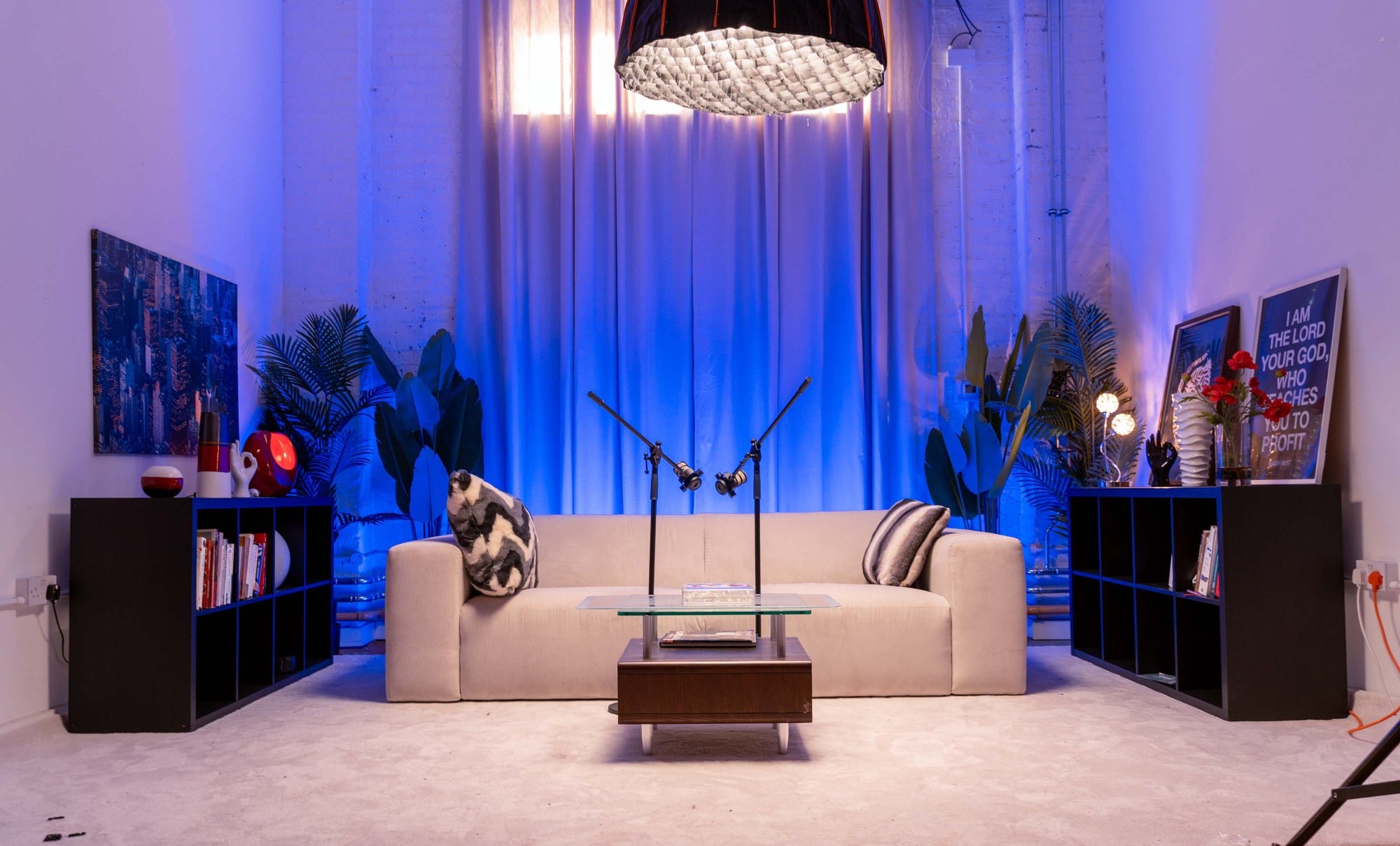 The same sofa and curtains lit deep blue, with a gridded softbox overhead and the shelves either side